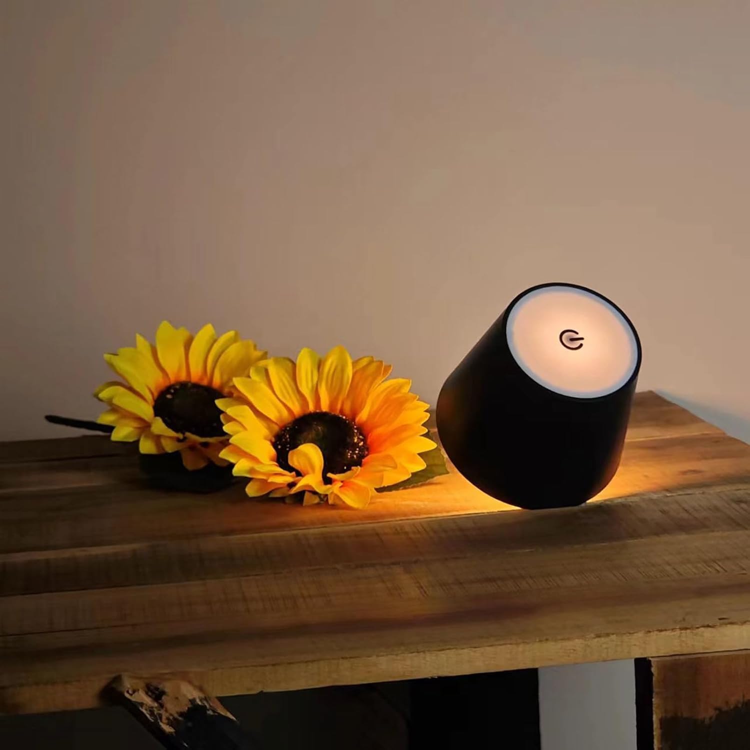 Black candle with a white wick on a wooden surface next to two sunflowers.